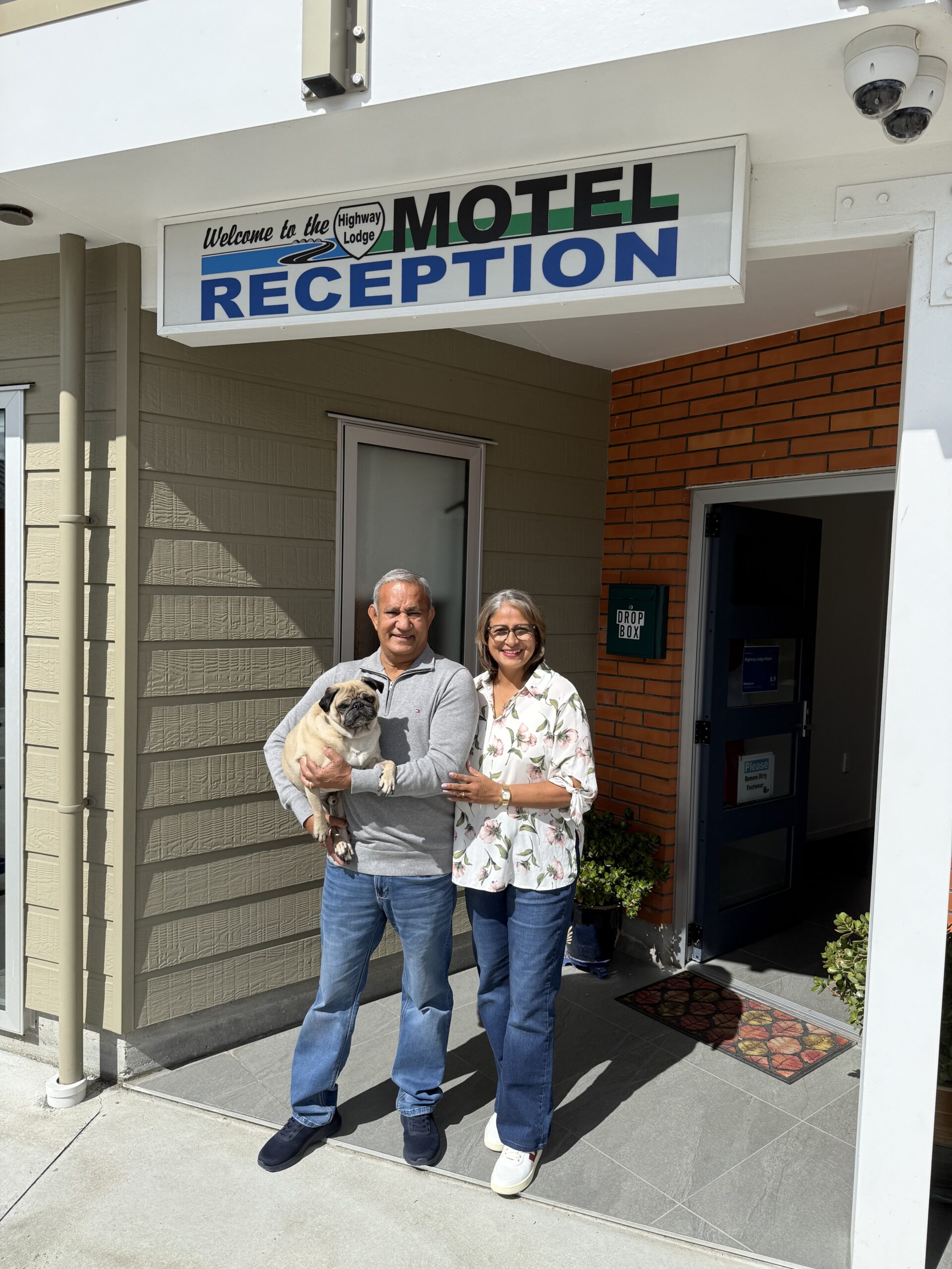 Highway Lodge Motel Owners Photo of Prem and Sharada with their dog Doug standing outside Highway Lodge Motel's reception